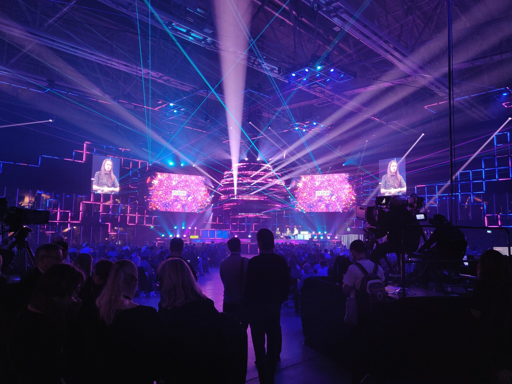 Slush conference main stage in Helsinki with dramatic purple and pink lighting, laser beams, and a packed audience