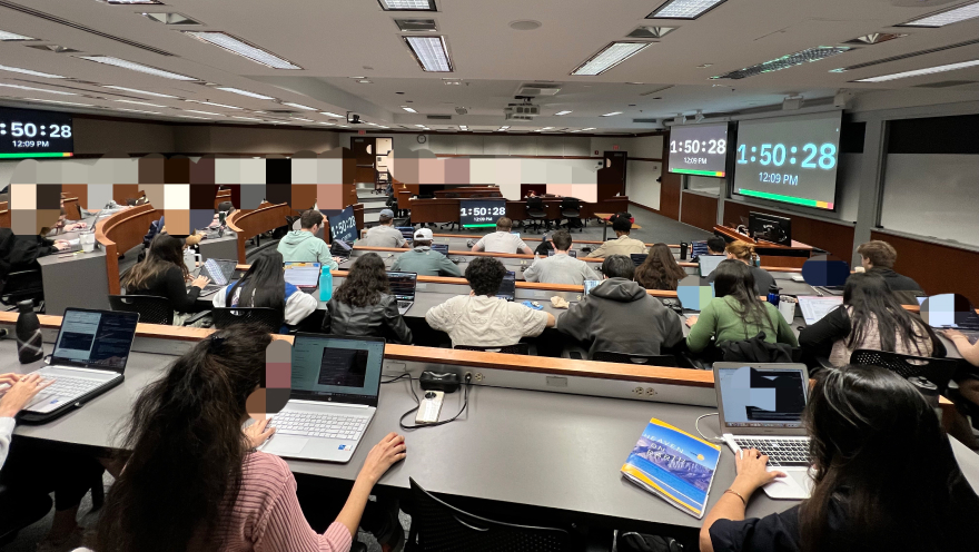 University lecture hall with students taking exam and multiple screens showing 1:50:28 timer